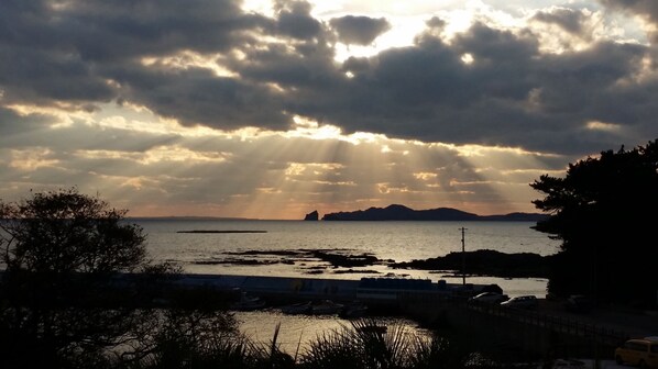 Vista costera con un puerto deportivo, barcos y el silueta de una isla distante bajo un cielo nublado.