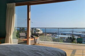 A balcony with a view of the sea and boats, a bed, and a chair. - JEJU Doldam B&B (Seogwipo)
