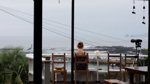 A view from a balcony overlooking a body of water with boats, a lighthouse, and distant landforms. - JEJU Doldam B&B (Seogwipo)