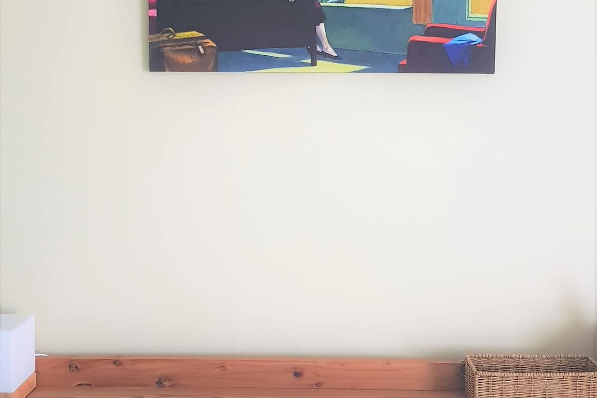 Un tableau représentant une femme assise près d’une fenêtre, avec une vue sur un paysage.