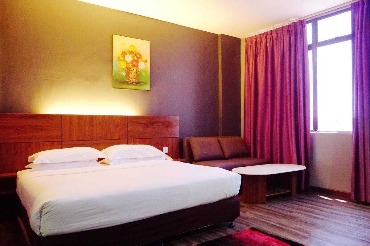 A hotel room with a bed, a small table, a sofa, and a painting on the wall.
