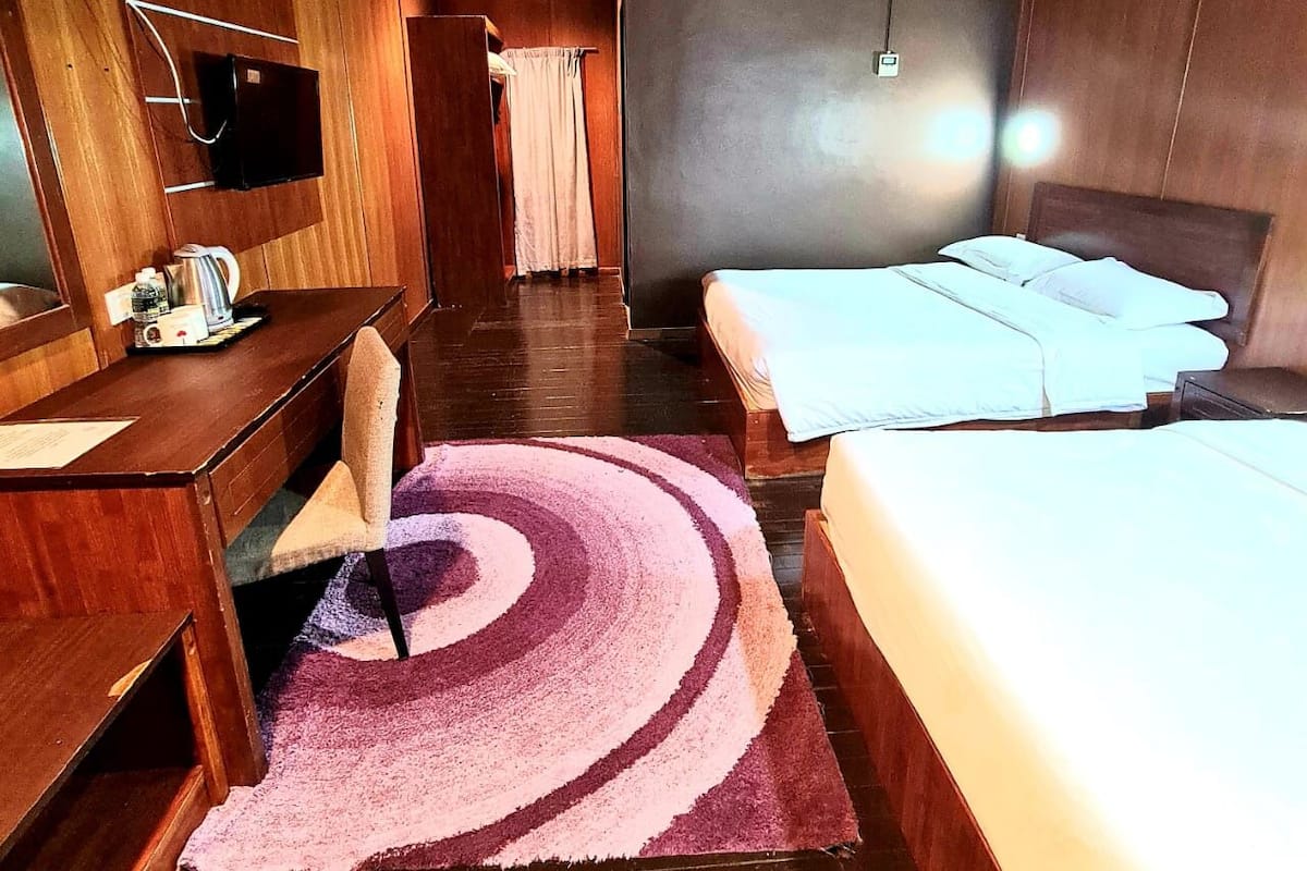 A hotel room with a wooden interior, a desk with a chair, a bed, a TV mounted on the wall, and a bathroom visible through a door.
