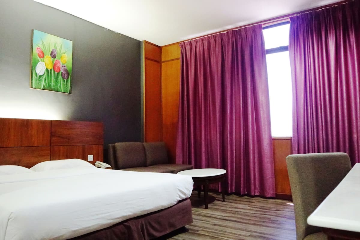 A hotel room with two beds, a small table, a chair, and a painting of flowers on the wall.