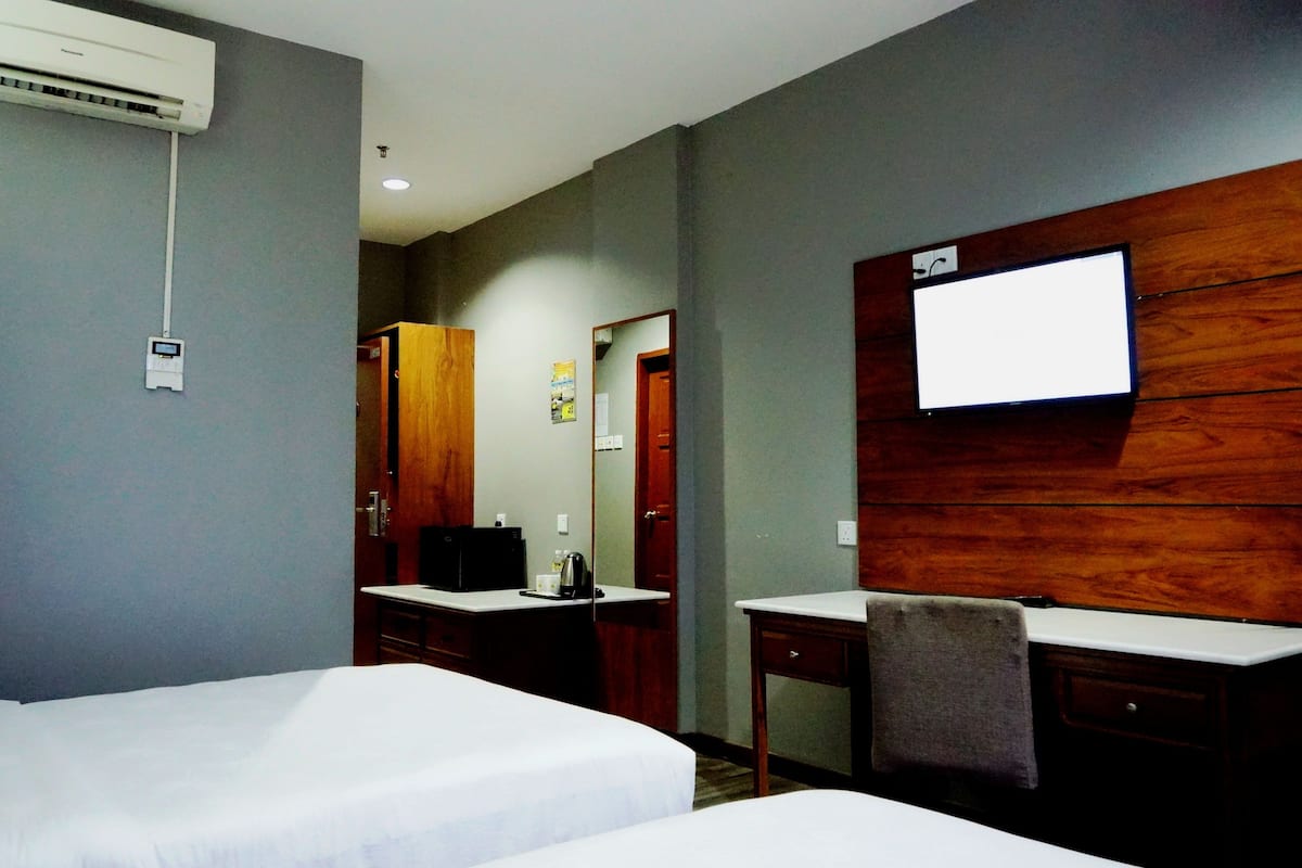 A hotel room with two beds, a desk with a chair, a TV mounted on the wall, and an air conditioning unit.