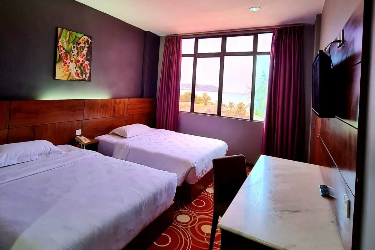A hotel room with two beds, a desk, a TV, and a window with a view.