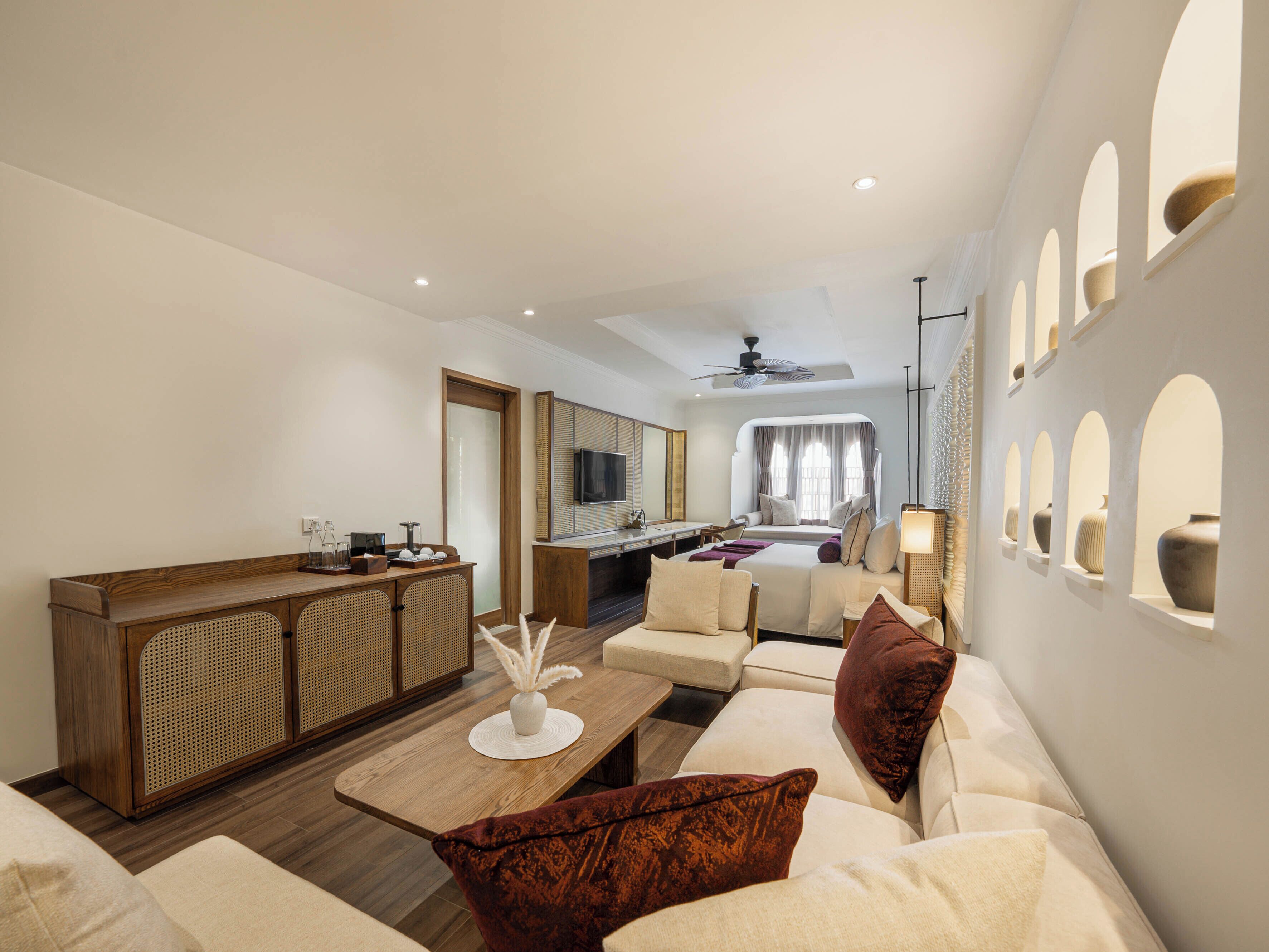 A modern hotel room with a living area, a dining space, and a bedroom with a large window.