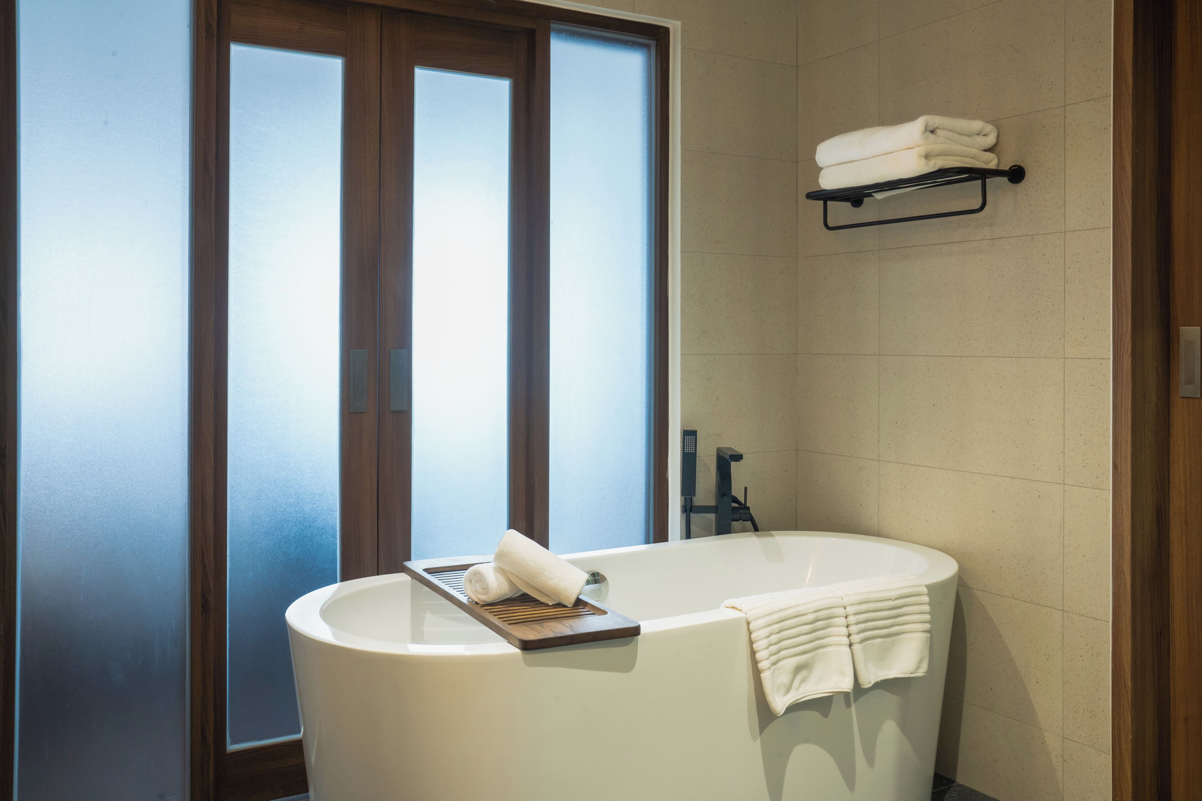 Un baño moderno con una bañera independiente, un perchero sobre la bañera y un ventanal con vidrio esmerilado.