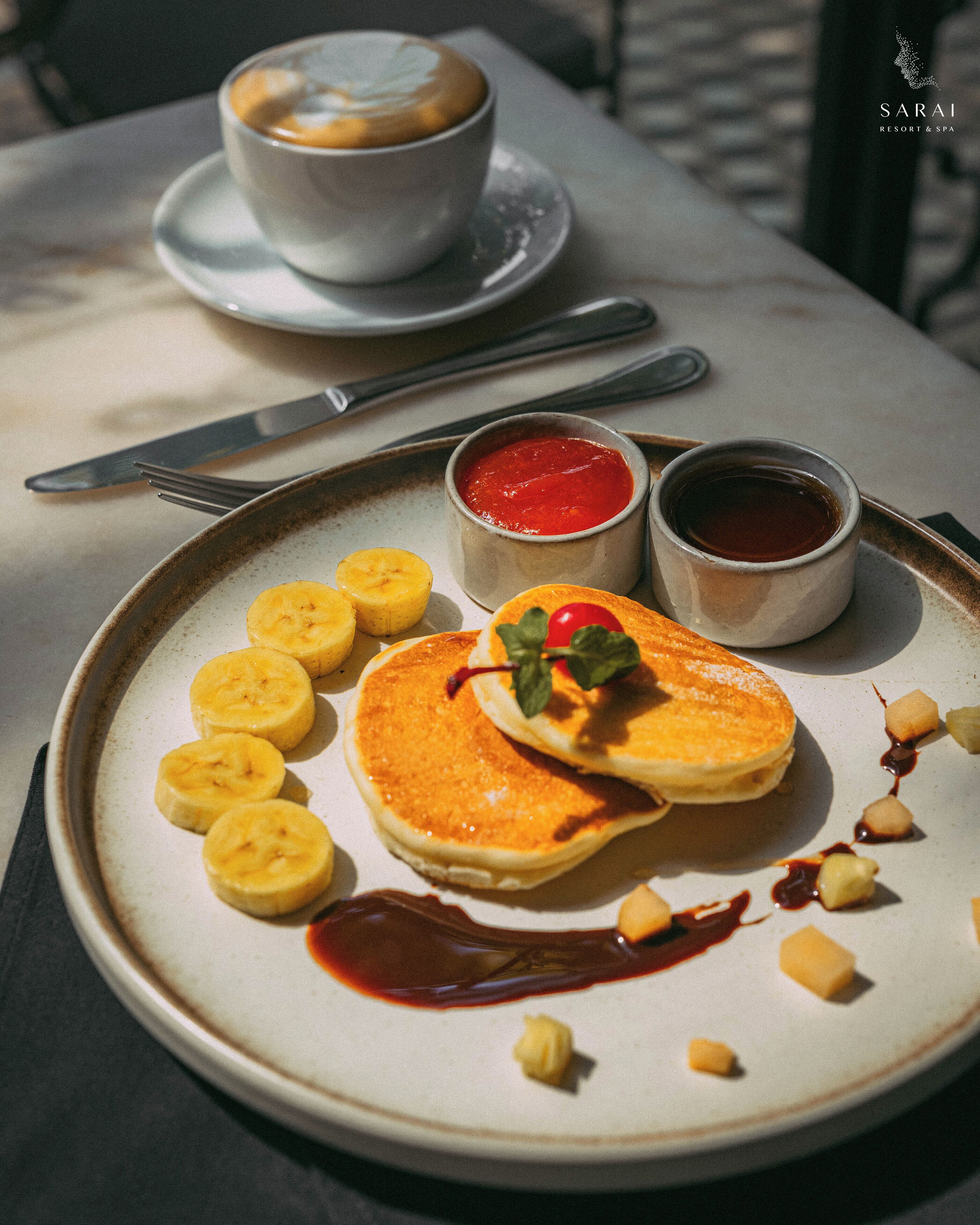 Une assiette de petit-déjeuner avec des crêpes, des tranches de banane et divers accompagnements.