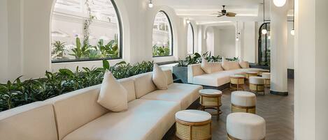 A modern lounge area with a sofa, ottomans, and wicker chairs.
