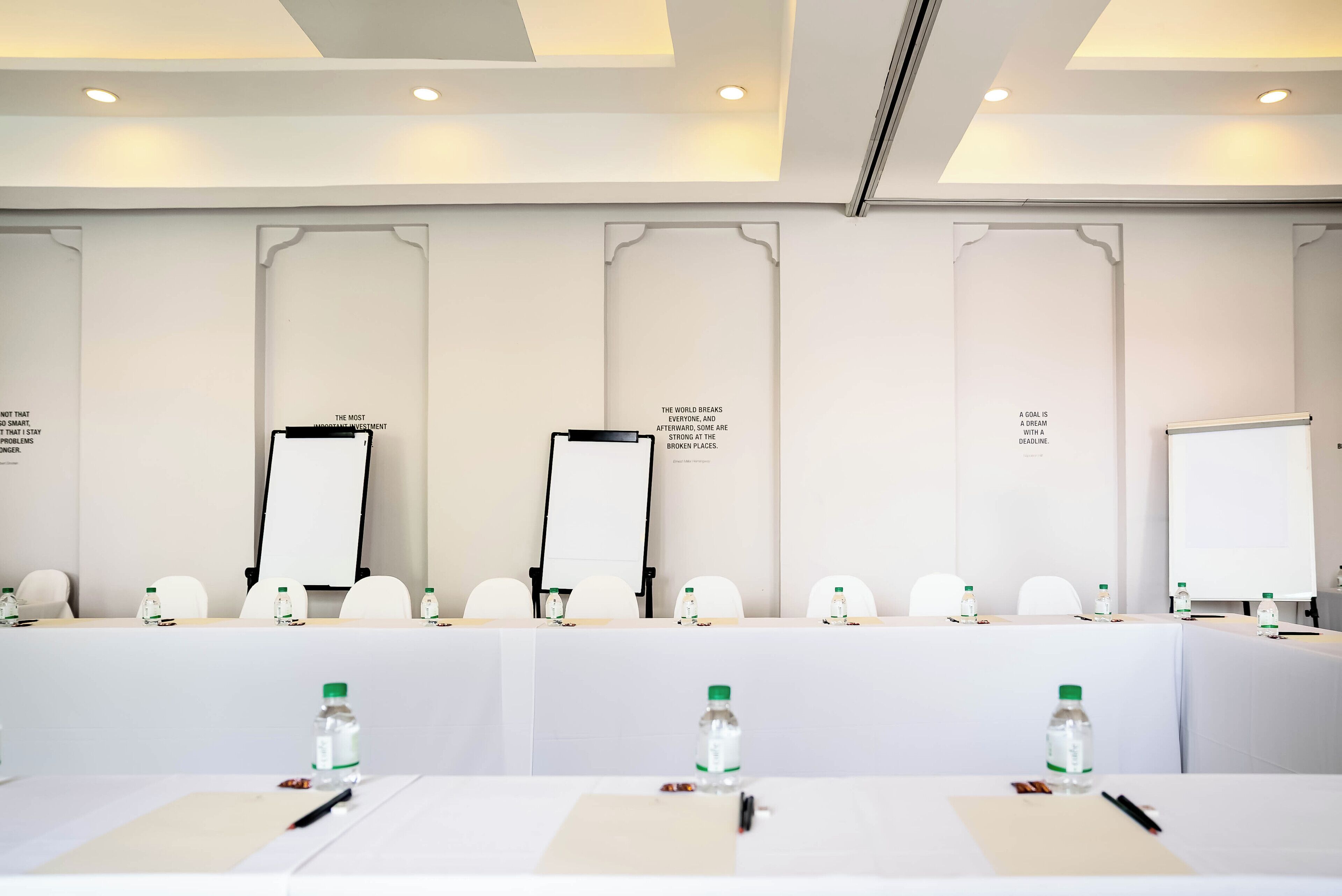 A conference room with a long table, white chairs, flip charts, and water bottles.