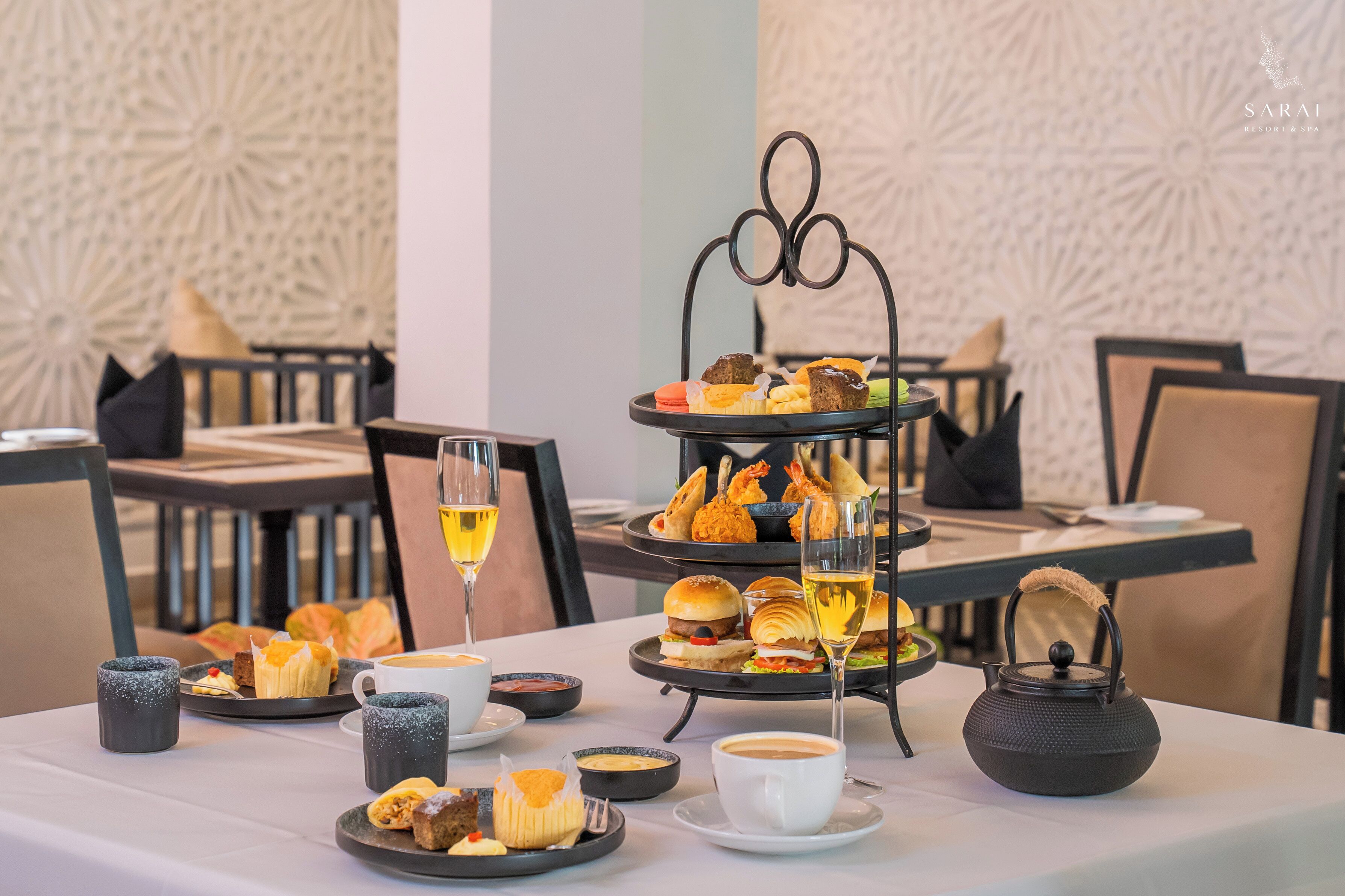 Une table à manger avec un présentoir à étages pour les desserts, des assiettes remplies de nourriture et une théière.