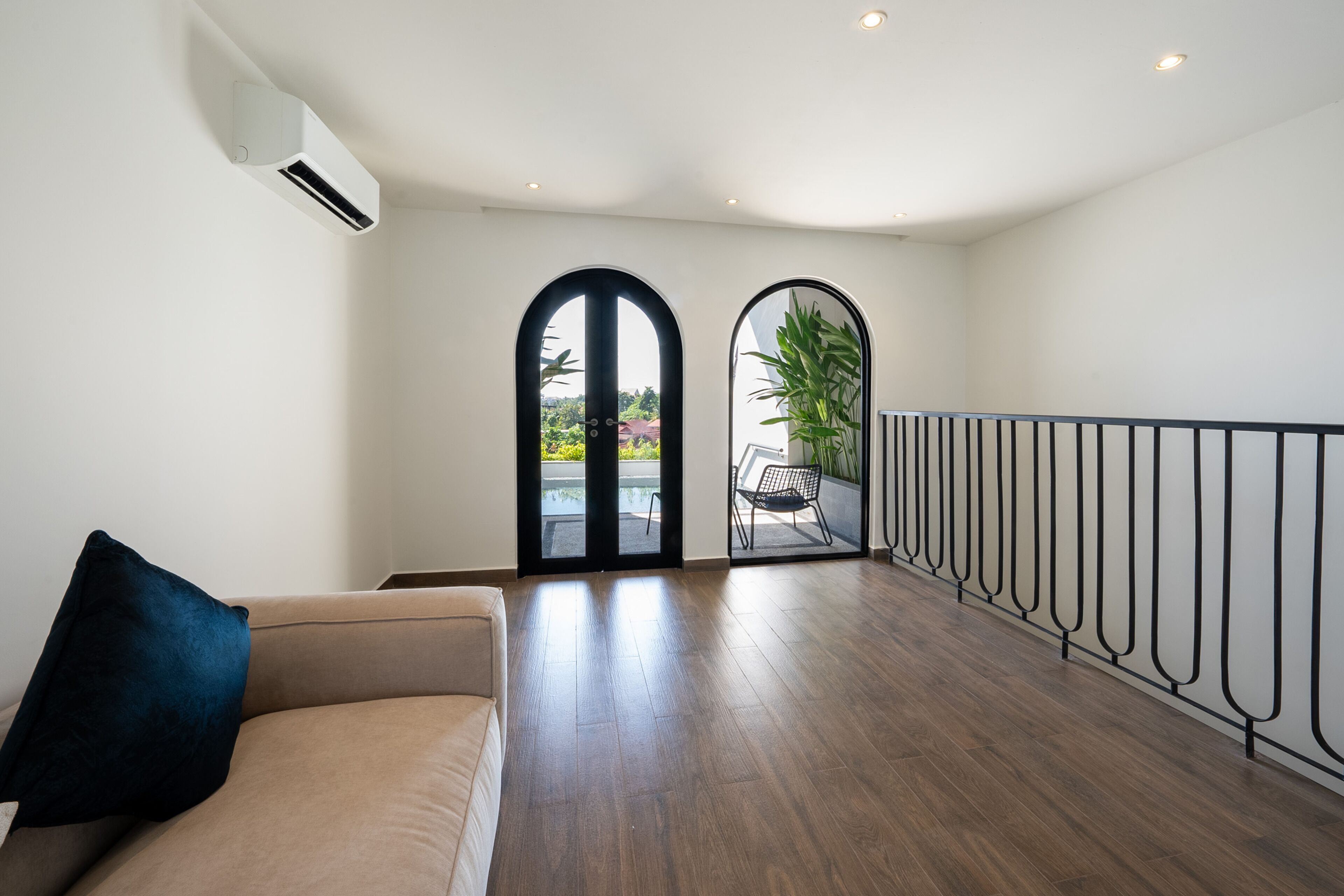 A spacious room with a beige sofa, a black-framed window, and a view of an outdoor area with a chair and plants.