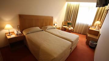 Une chambre d’hôtel avec deux lits, un bureau, une chaise, une télévision et une fenêtre avec des rideaux.