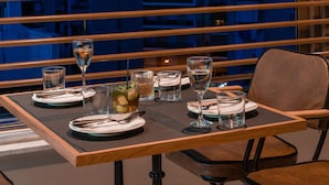 Mesa de comedor dispuesta con vasos y cubiertos, con vistas a un paisaje urbano y un edificio destacado.
