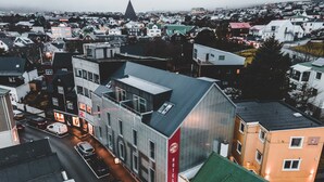 Een hotel met een modern ontwerp, met een opvallend rood bord, gelegen in een dichtbebouwd stedelijk gebied met verschillende gebouwen en een zichtbare kerktoren op de achtergrond.