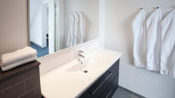 Un baño moderno con un lavamanos blanco, tocador de tonos oscuros y un espejo grande.