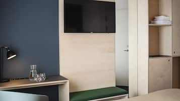 Una habitación de hotel moderna con una cama, un escritorio con lámpara, un televisor montado en la pared y un armario.