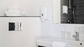 Une salle de bain moderne avec un lavabo blanc, un meuble noir, un porte-serviettes avec des serviettes pliées, un distributeur de savon et un espace douche équipé d’un pommeau de douche à main.