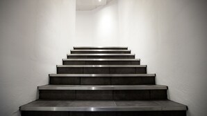 Een modern vormgegeven trap, gemaakt van donkere materialen, die omhoog leidt in een smalle ruimte met witte muren.