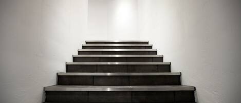 A staircase with a modern design, made of dark materials, leading upwards in a narrow space with white walls.