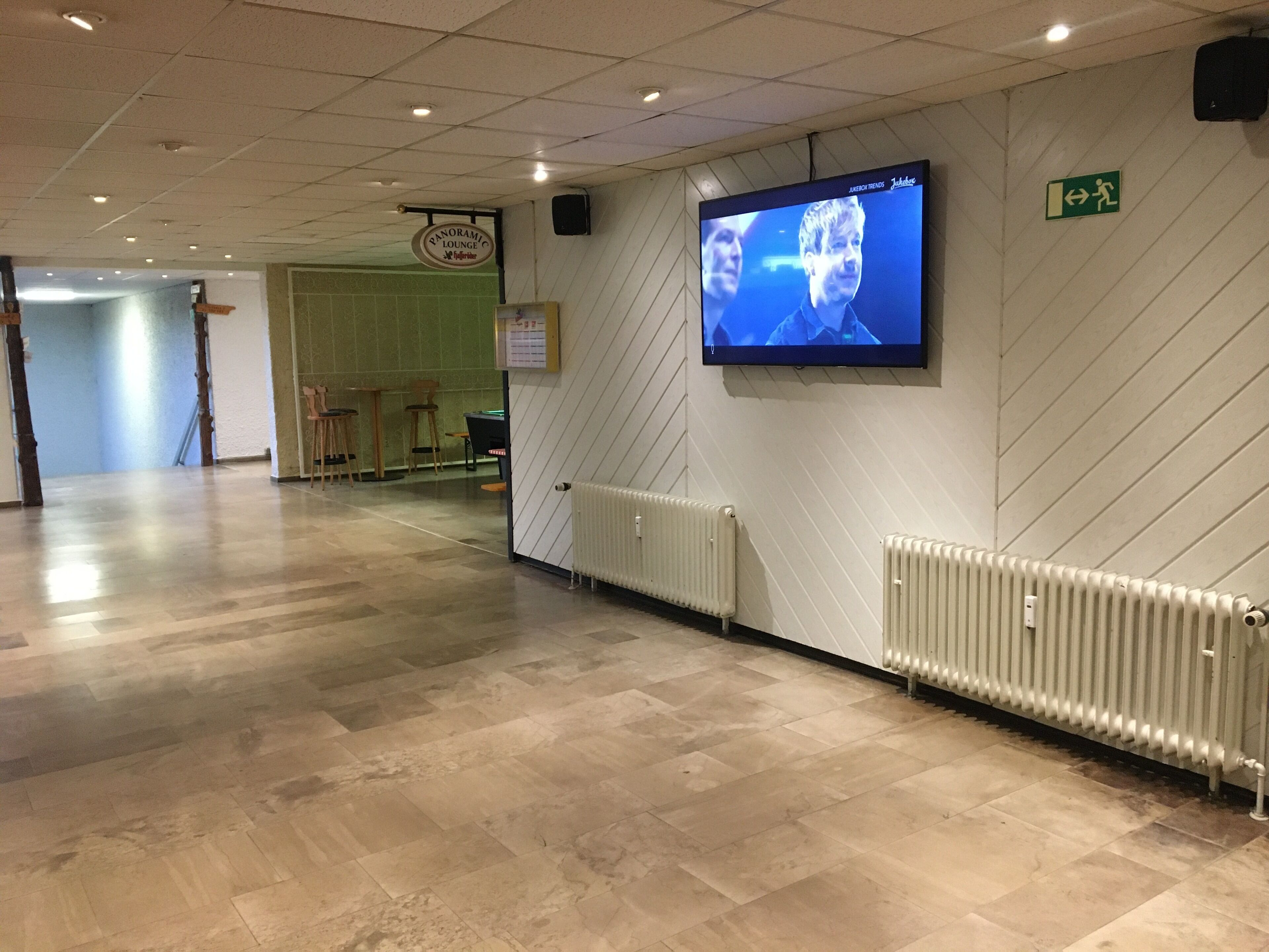 Un pasillo con una pantalla de televisión, un letrero que indica el Panorama Lounge y un letrero de salida de emergencia verde.