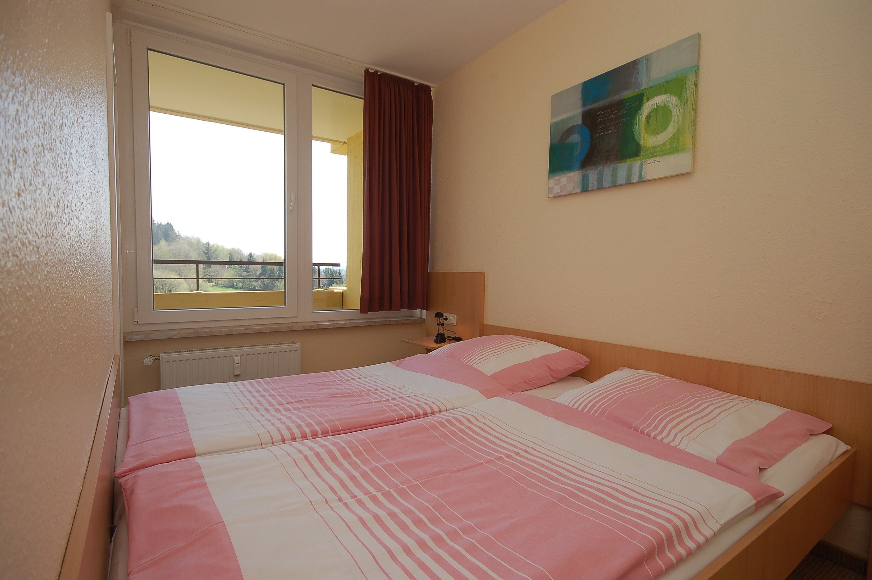 Een kamer met twee bedden, een raam met gordijnen, een radiator en een schilderij aan de muur.