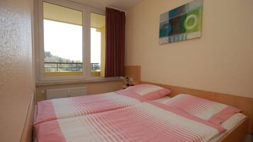 Een kamer met twee bedden, een raam met gordijnen, een radiator en een schilderij aan de muur.