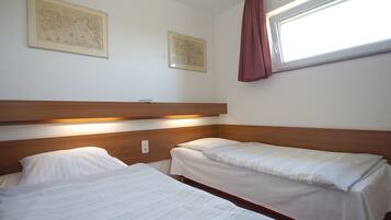 A room with two single beds, wooden headboards, white bedding, and two framed pictures on the wall.