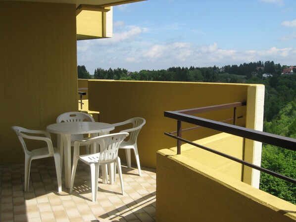 A balcony with a table and chairs, a railing, and a view of a green landscape with trees and houses. - Ferienapartments Panoramic Oberharz (Braunlage)