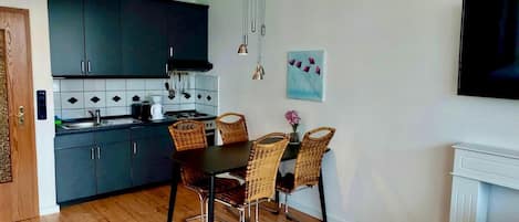 Una cocina compacta con armarios oscuros, una encimera negra y una zona de comedor con sillas de mimbre y una mesa.