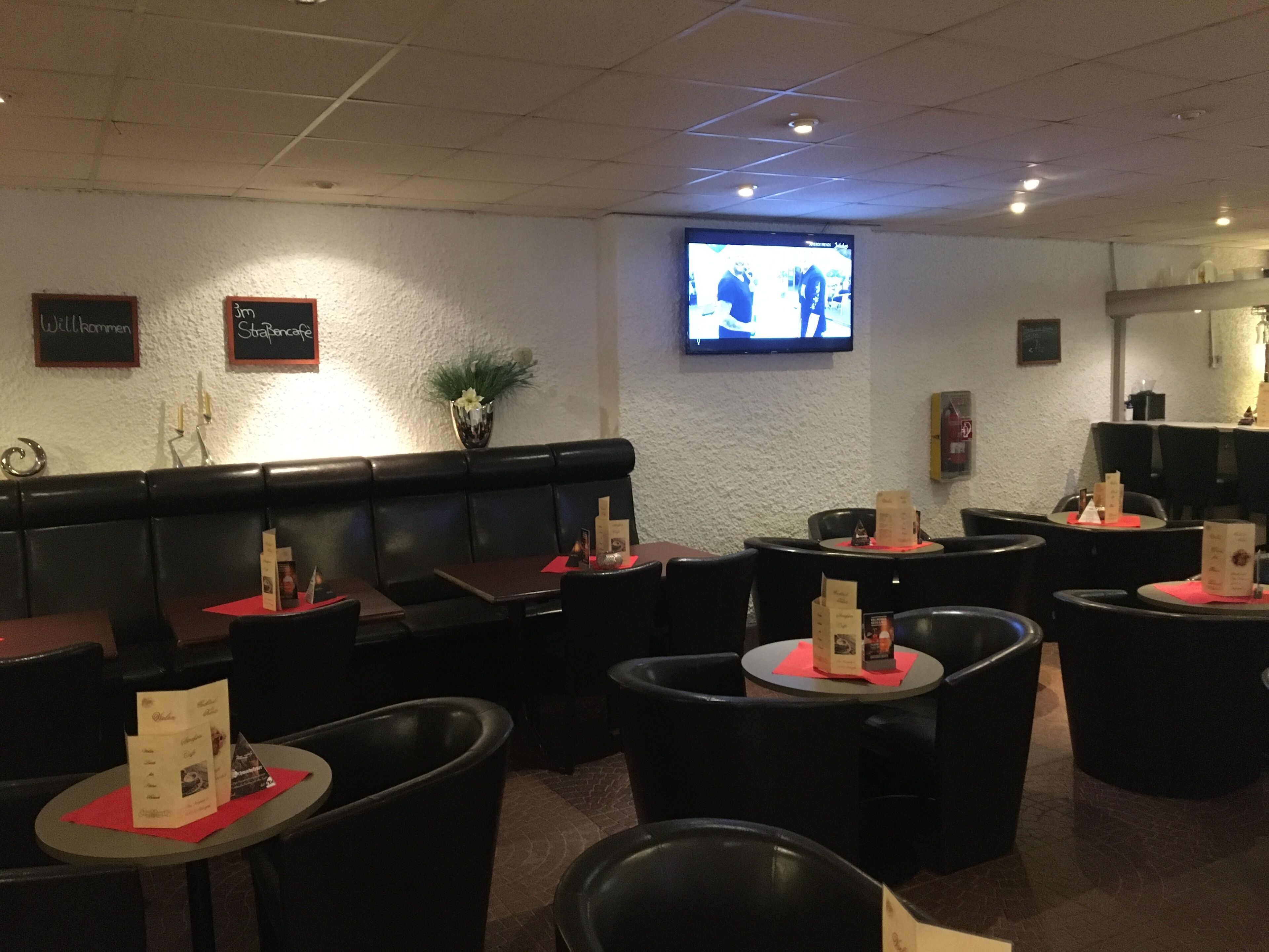 Un interior de restaurante con cabinas, mesas redondas y un televisor montado en la pared.