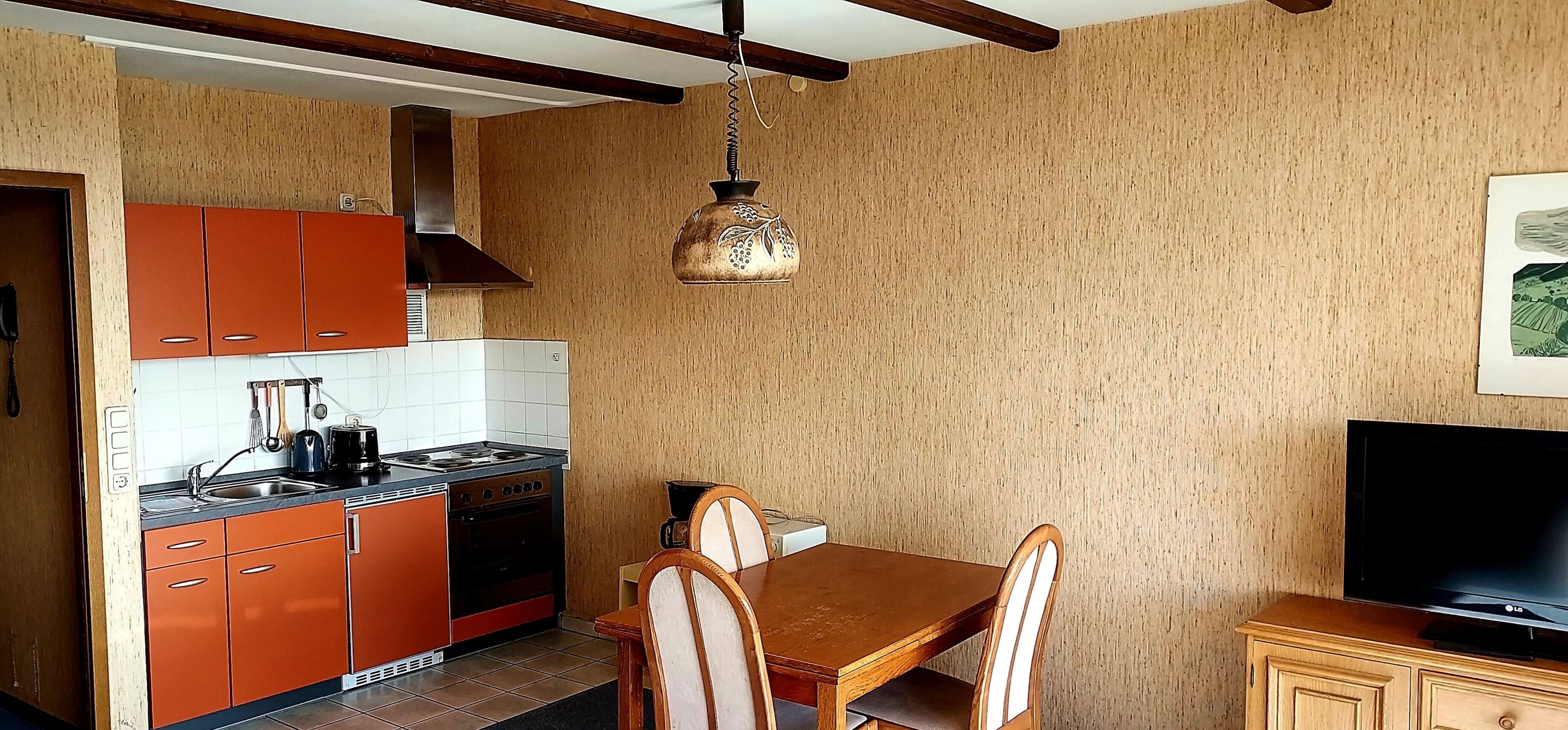 A compact kitchen with orange cabinets, a stove, and a dining area with a table and chairs.