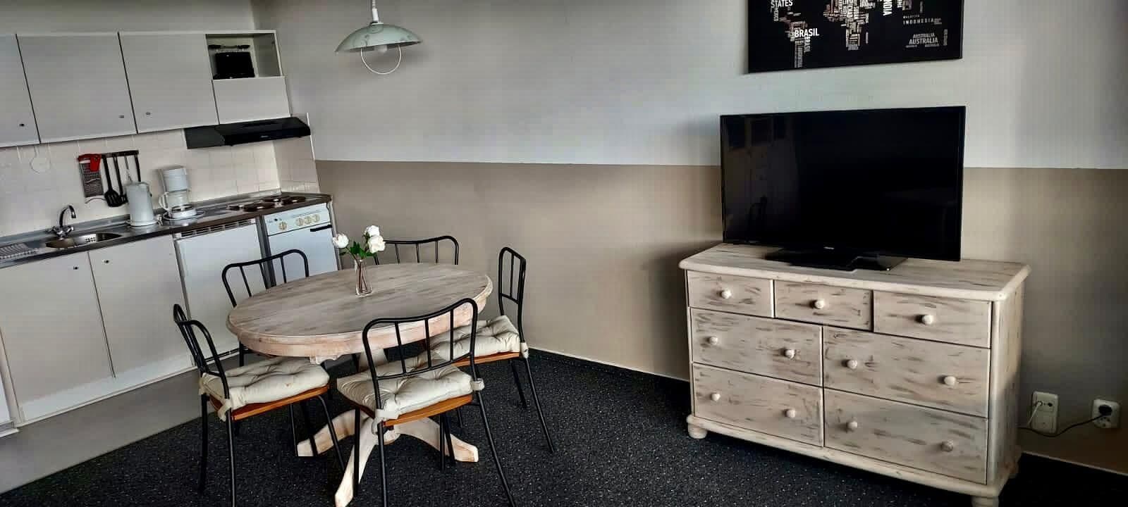 A compact kitchen with a dining table and chairs, a TV, and a dresser.