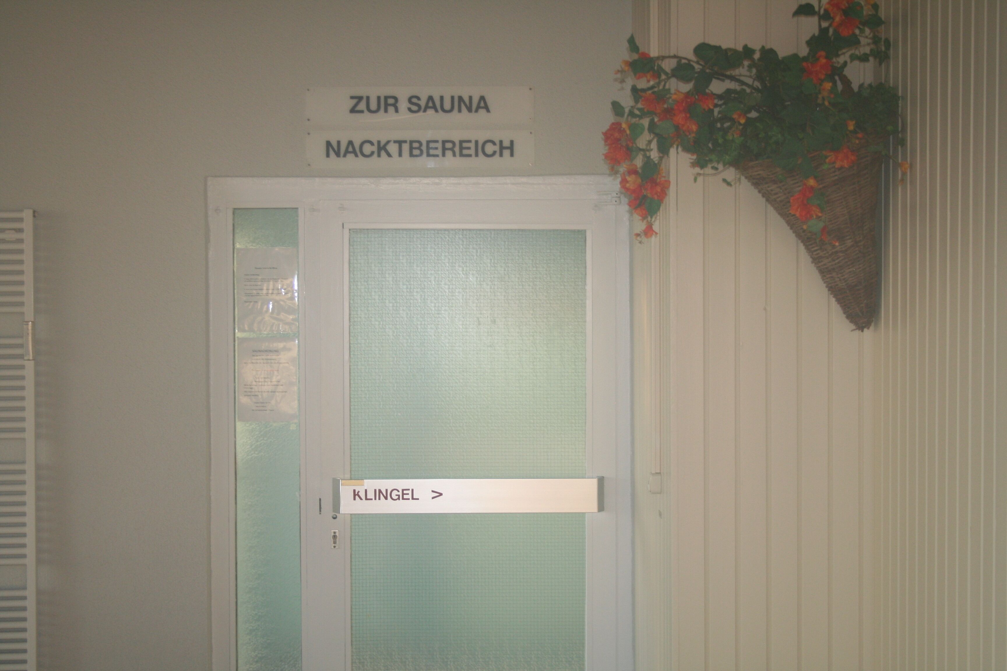 Une porte portant l’inscription « Zur Sauna Nachtbereich », avec un panneau en verre dépoli et une sonnette située en dessous.