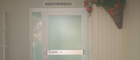 Une porte portant l’inscription « Zur Sauna Nachtbereich », avec un panneau en verre dépoli et une sonnette située en dessous.