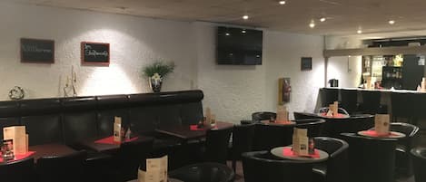 Ein Restaurant mit Sitzbänken und Tischen, einem Flachbildfernseher an der Wand und einer Bar im Hintergrund.