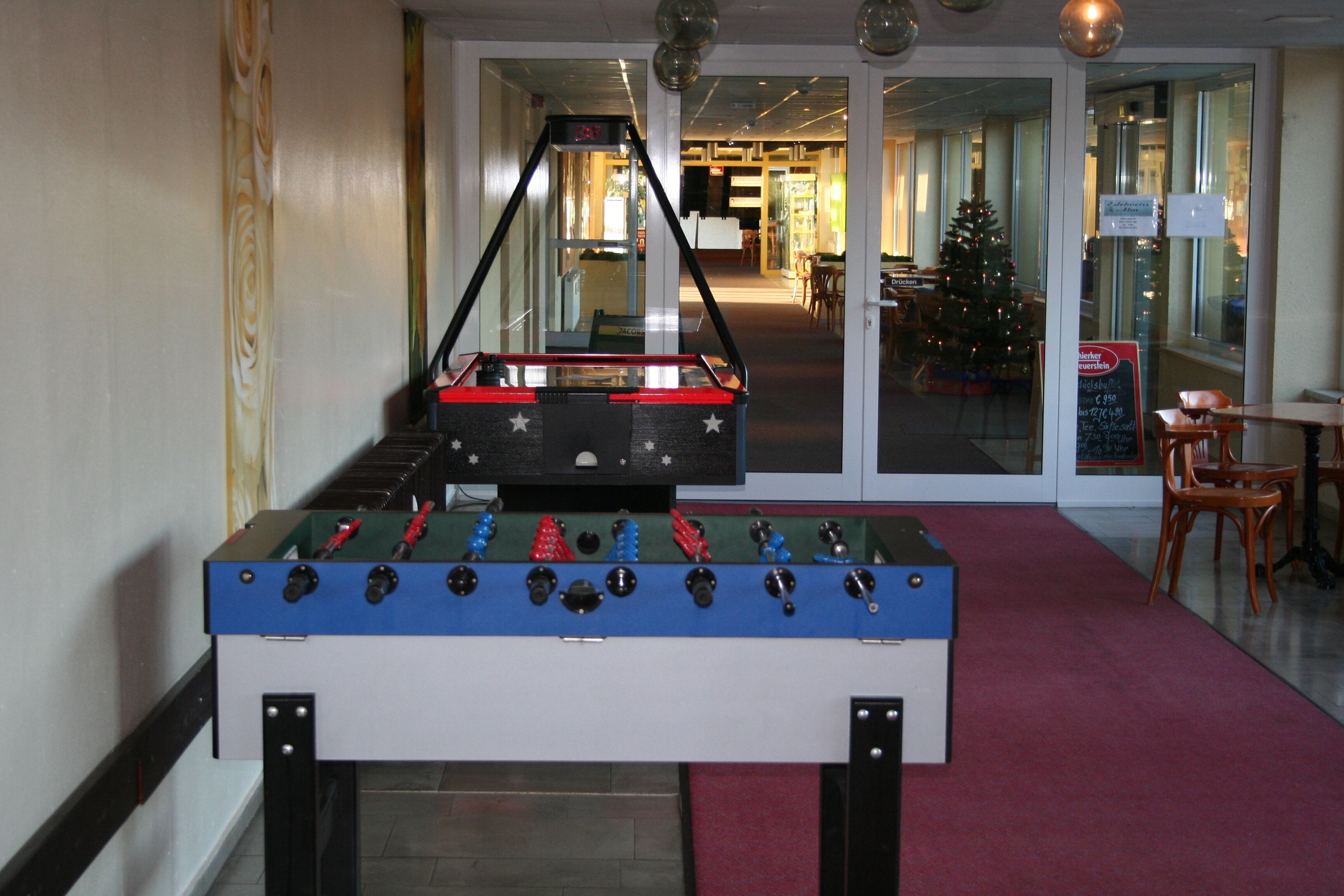 A foosball table in a hotel lobby with a red carpet, a Christmas tree, and a signboard.