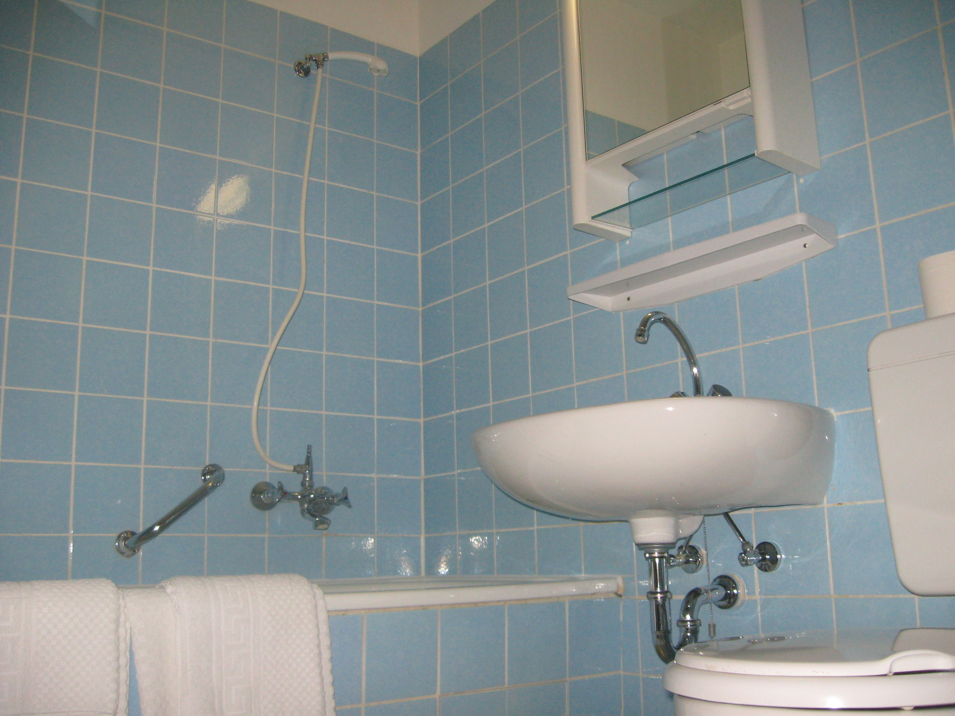 A bathroom with blue tiled walls, a white sink, a mirror, and a shower.
