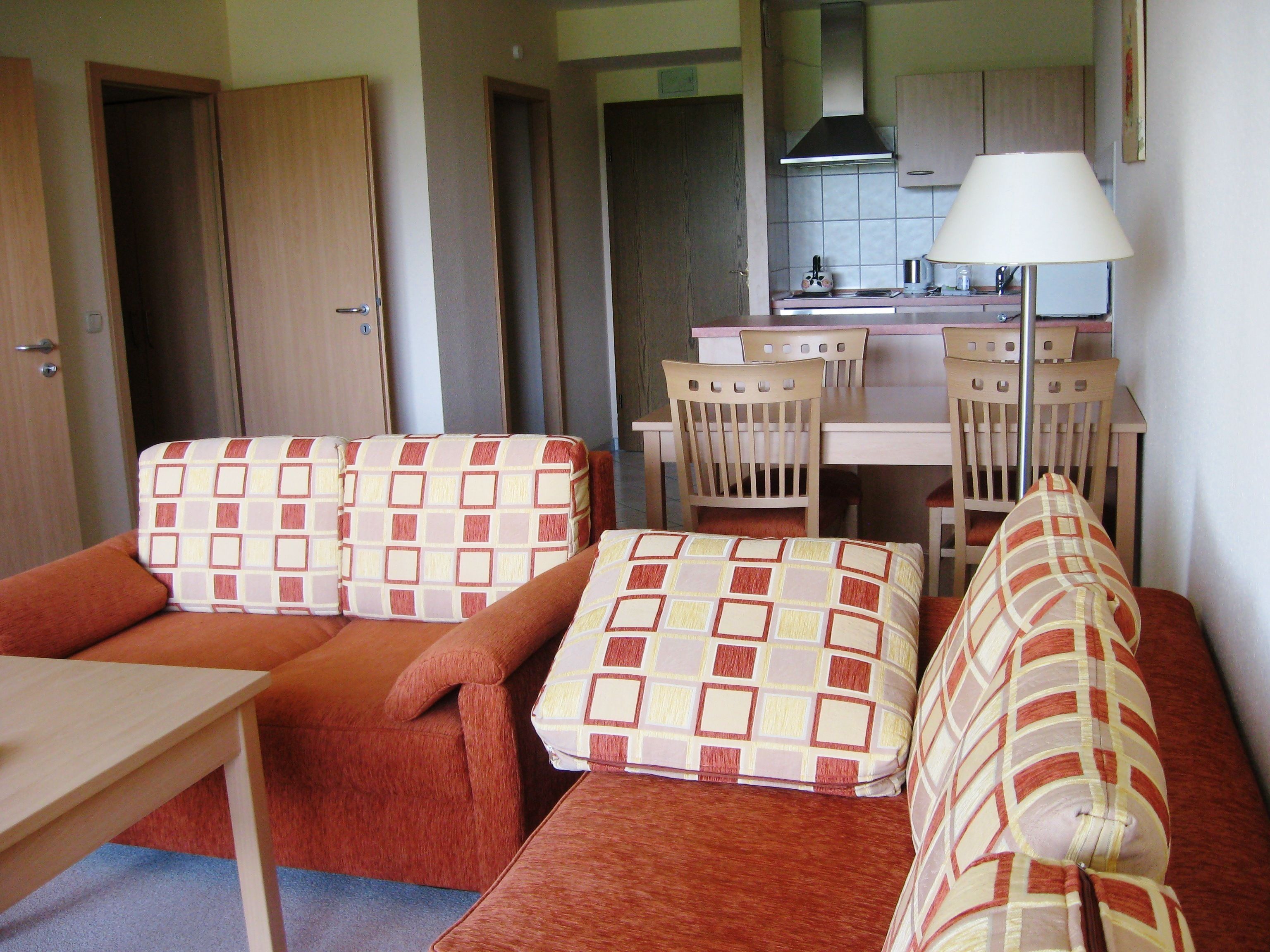 A compact living space with a sofa set, a dining table, and a kitchen area with a stove and a lamp.