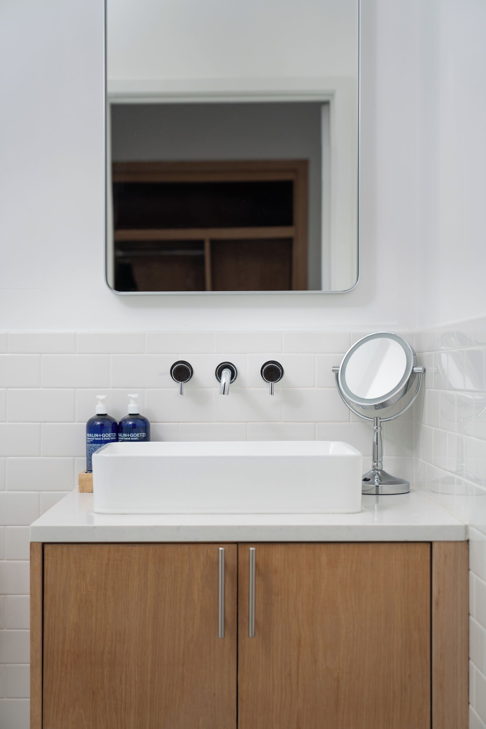 A bathroom with a white sink, wooden cabinets, a mirror, and two bottles of hand soap.