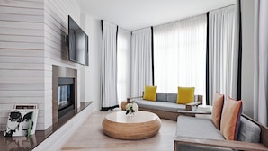 A modern living room with a fireplace, a round coffee table, a sofa with cushions, and a TV mounted on the wall. - Bungalow Hotel (Long Branch)
