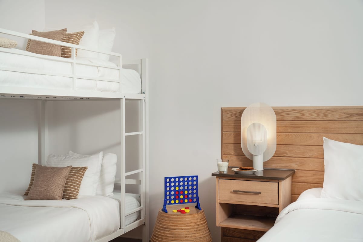 Ein Etagenbett mit Kissen, ein Nachttisch aus Holz mit einer Lampe und ein kleiner Hocker mit einem Gesellschaftsspiel.
