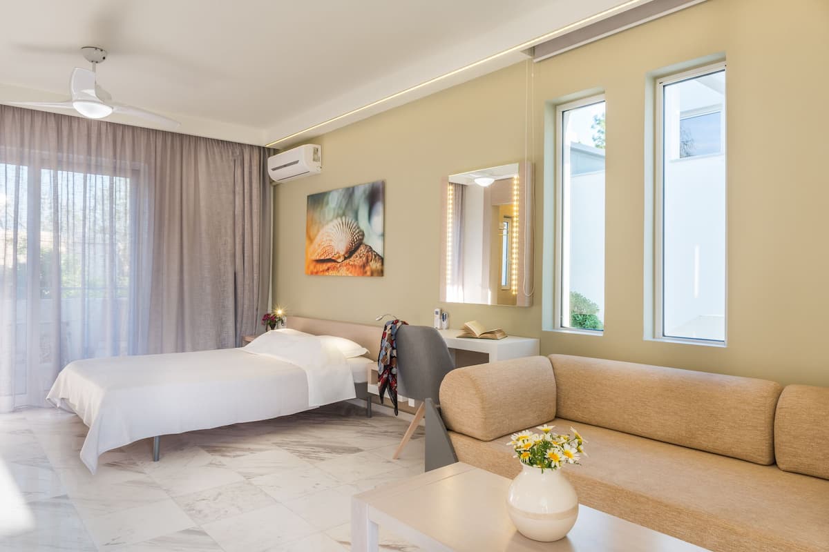 A hotel room with a bed, a sofa, a desk, and a large window.