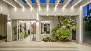 A modern building entrance with glass doors, indoor plants, and a blue-lit ceiling.