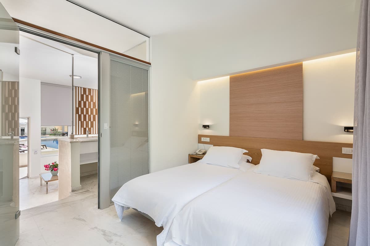A modern hotel room with a large bed, a bedside table, a nightstand, and a view of a pool area.