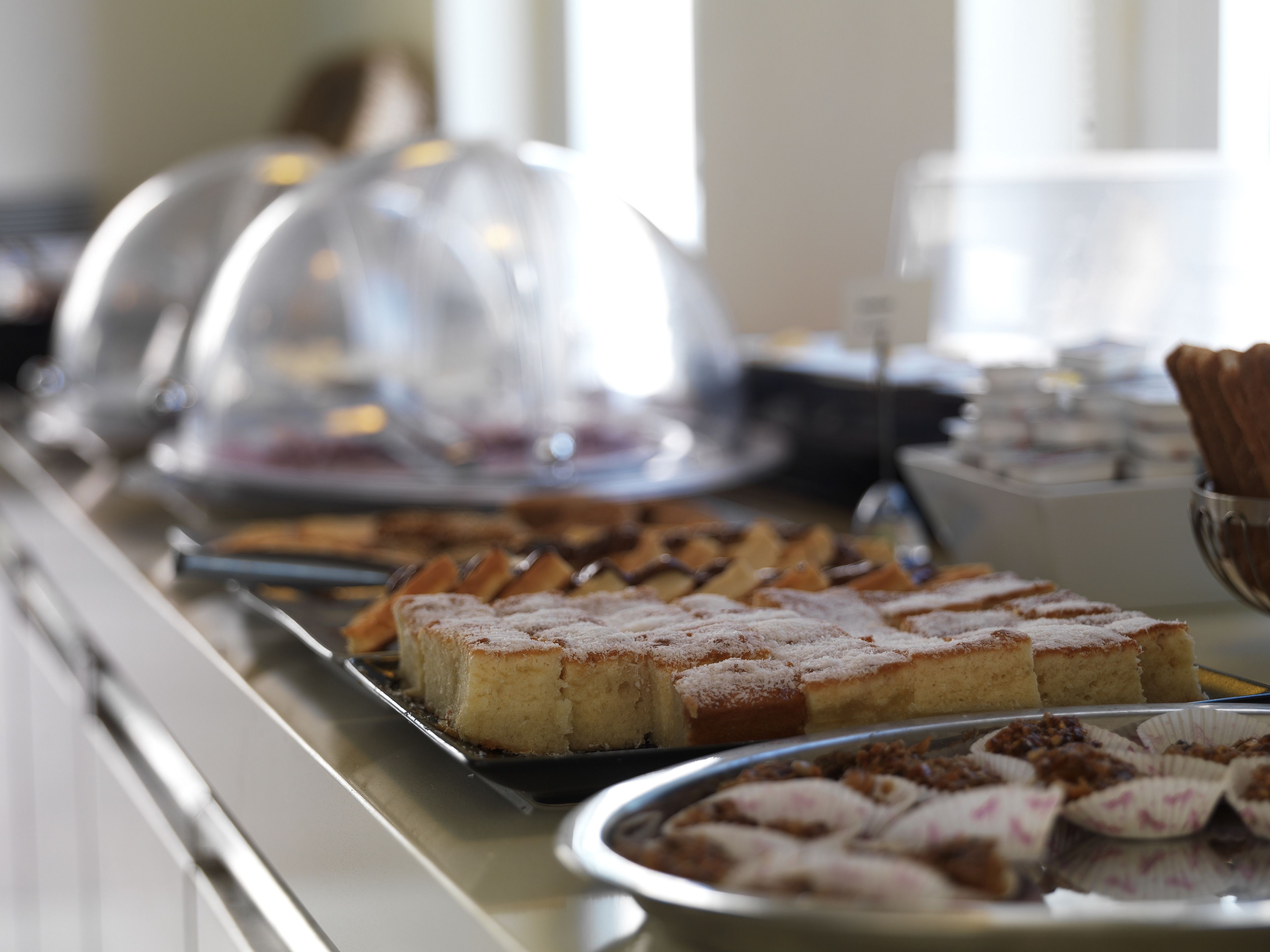 A buffet with various desserts and pastries, including cakes and tarts, displayed on trays.