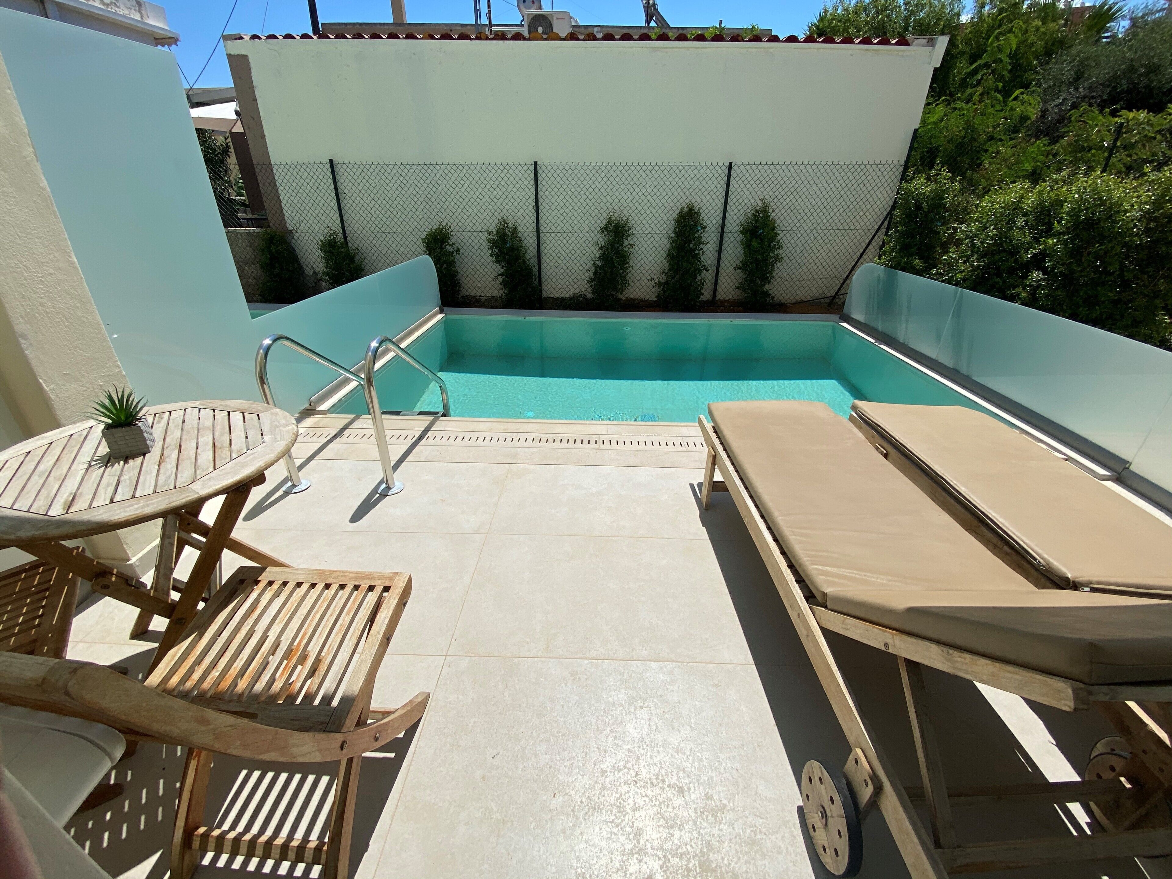 A rooftop pool area with a small table, a lounge chair, and a potted plant.