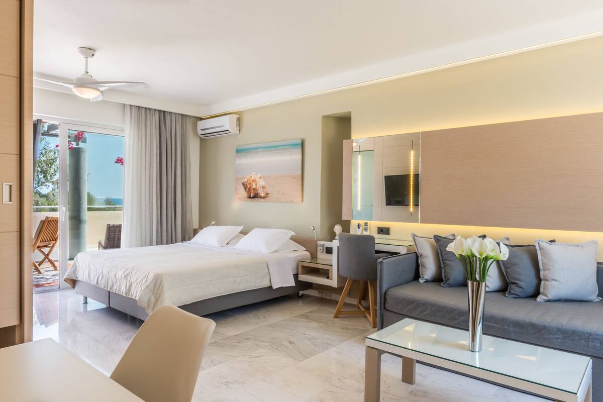 A modern hotel room with a bed, a sofa, a desk, and a glass coffee table.