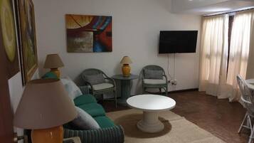 A living room with a sofa, two chairs, a round table, a TV, and a painting on the wall.
