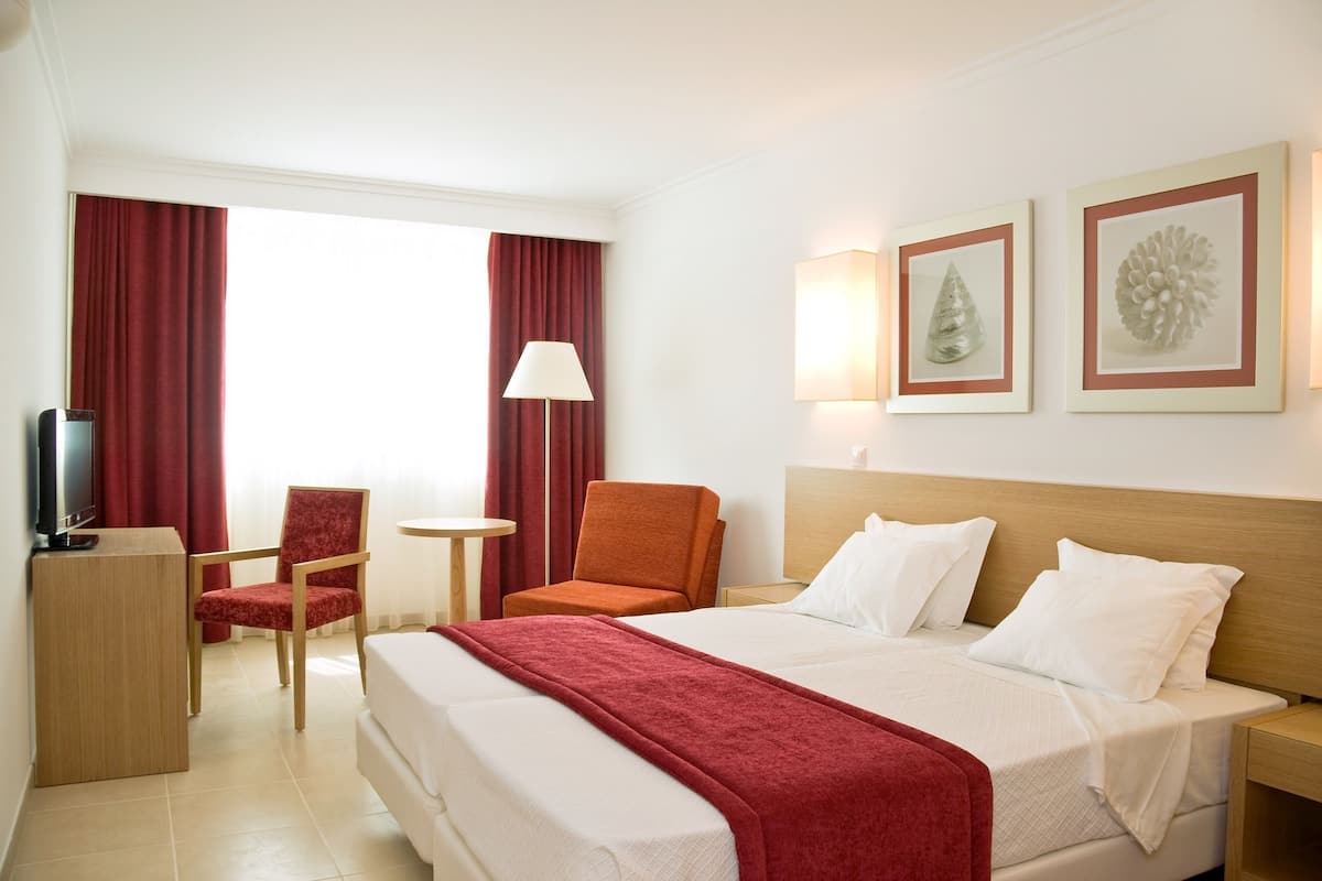 Ein Hotelzimmer mit einem Bett, zwei Stühlen, einem Schreibtisch, einem Fernseher und Bildern an der Wand.